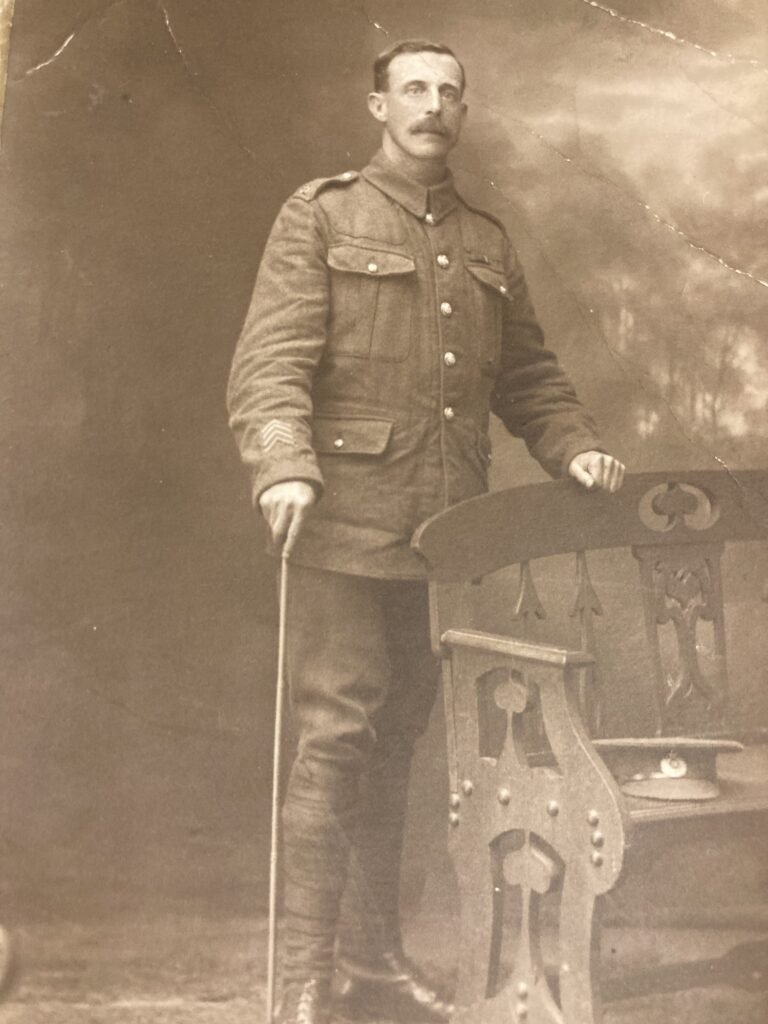 Sepia photograph of a soldier in uniform standing with a cane beside a carved bench