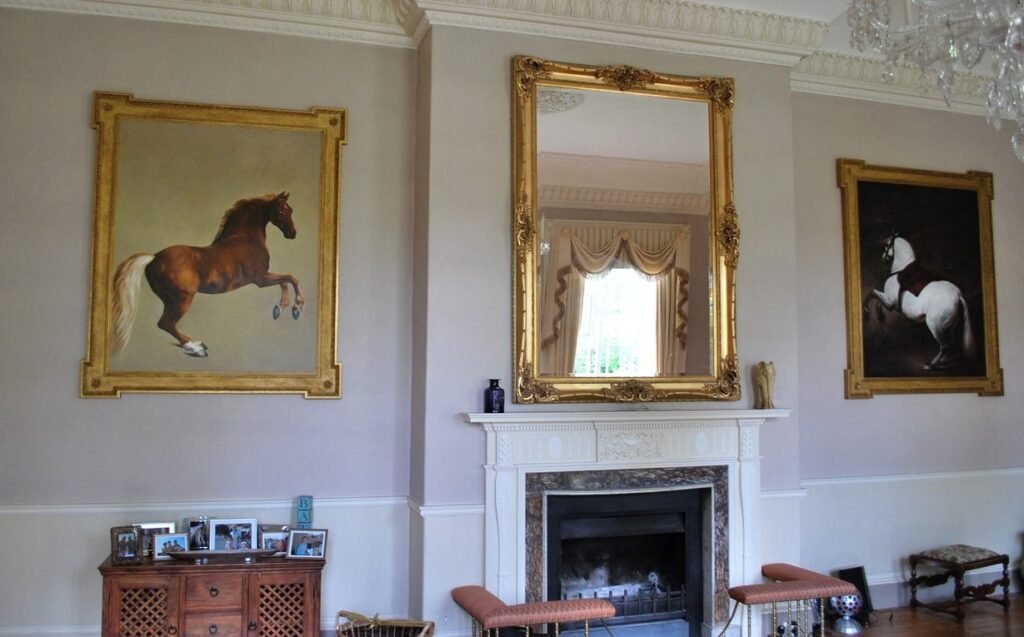 Two framed horse paintings either side of a gilt mirror above a fireplace