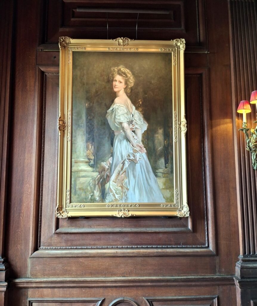 A portrait in an ornate gilt frame on a wood-panelled wall