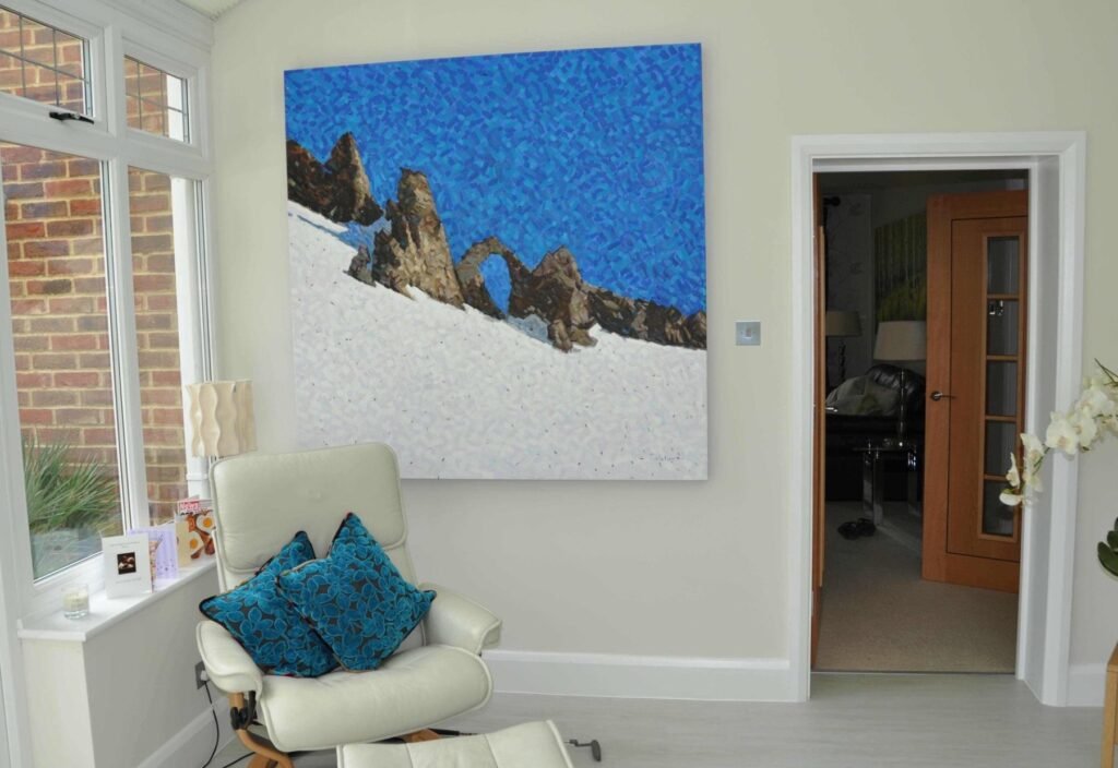 A blue mountain painting in a conservatory beside a white armchair