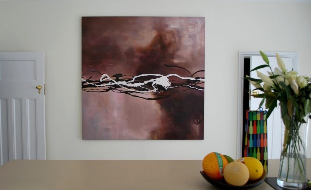 An abstract painting on a kitchen wall above a bowl of fruit and flowers