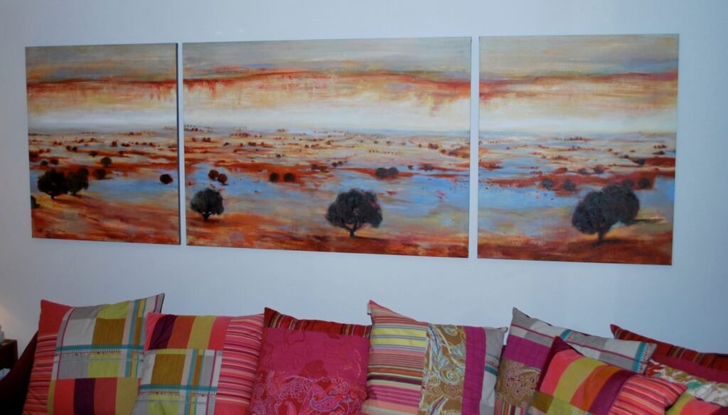 A landscape triptych above a sofa with colourful cushions